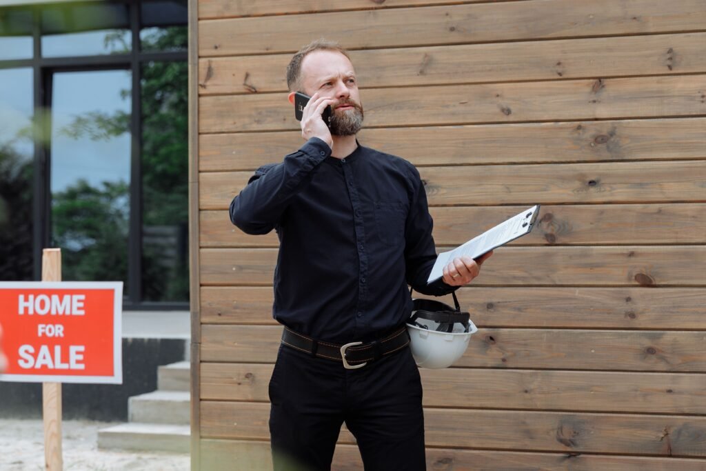 Real estate agent using a phone in front of a for-sale sign