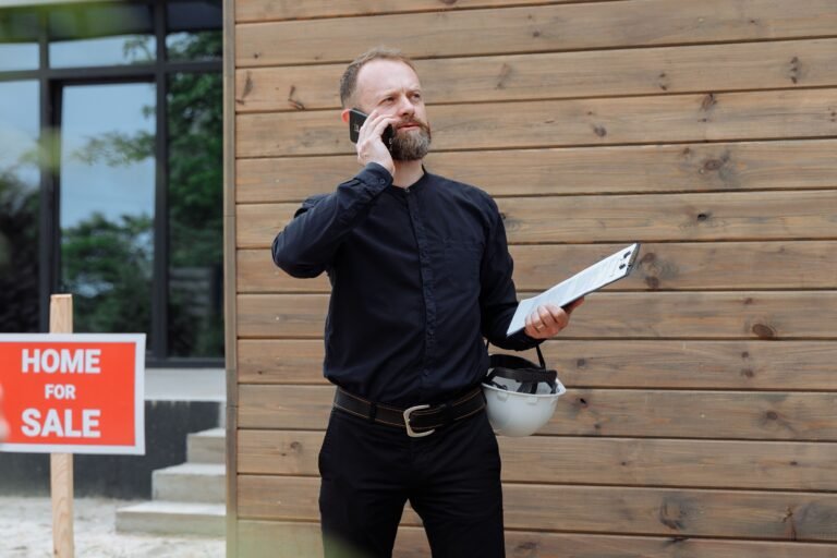 Real estate agent using a phone in front of a for-sale sign
